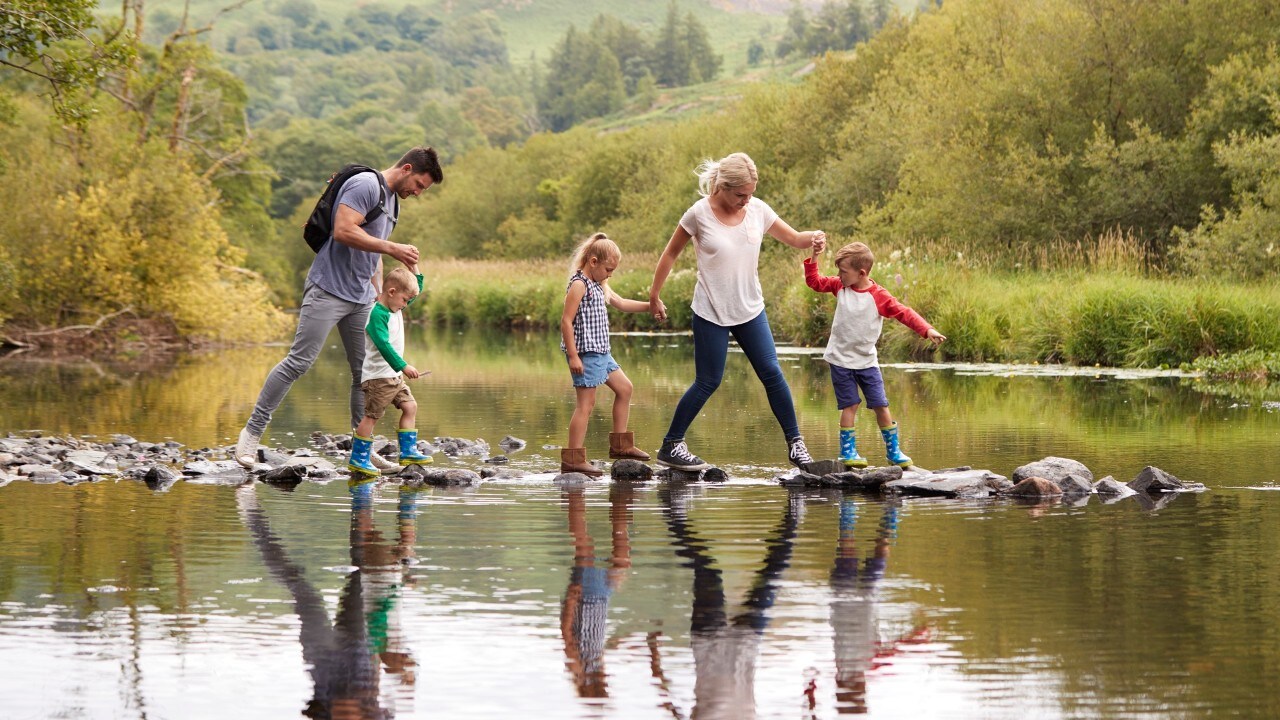 Family Crossing River Whilst Hiking In UK Lake District