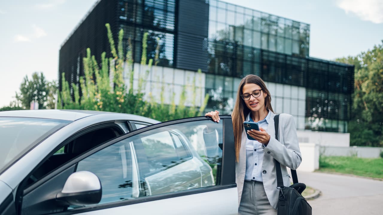 Frau am Telefon, die in ein Auto steigt.